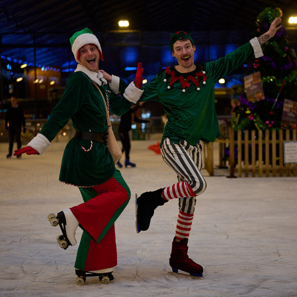 2 Elf skaters on ice with colourful red and green costuems