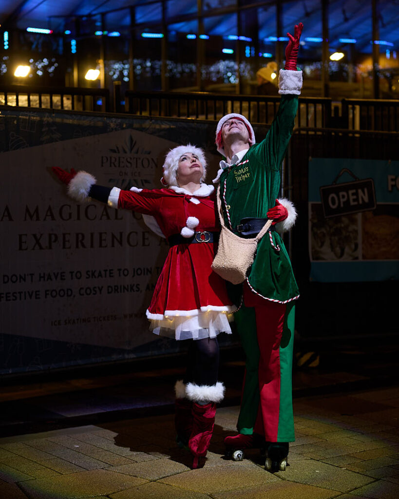2 rollerskaters wearing a Mrs Claus costume and Elf costume in reds and green