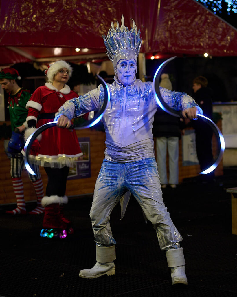 The Ice King in a white and shimery blue costume entertains Mrs Claus on rollerskates